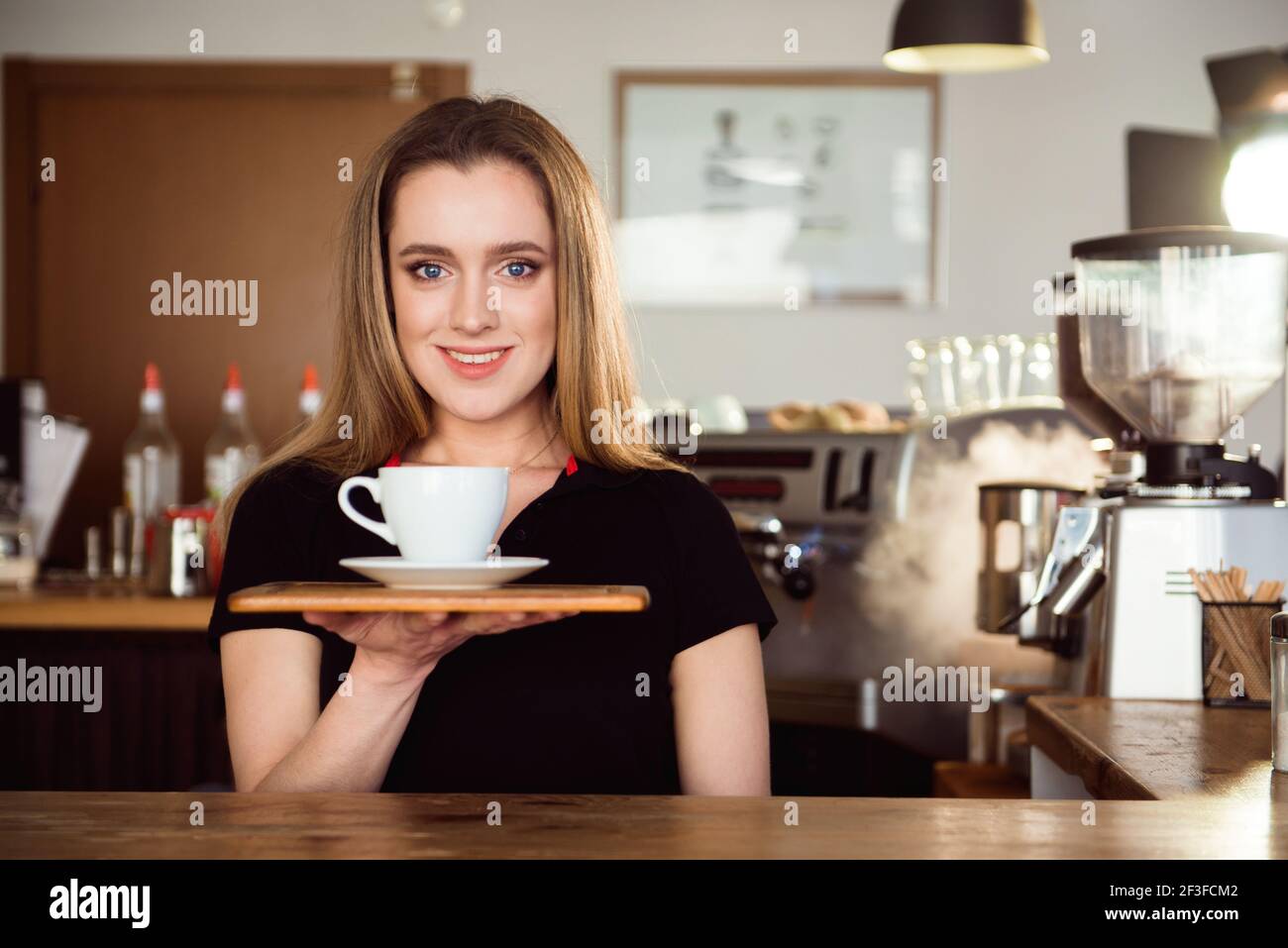 Hermosa mujer barista está trabajando en la cafetería. Una mujer atractiva  está de pie detrás del mostrador del bar, haciendo café y da la bienvenida  a los clientes Fotografía de stock -