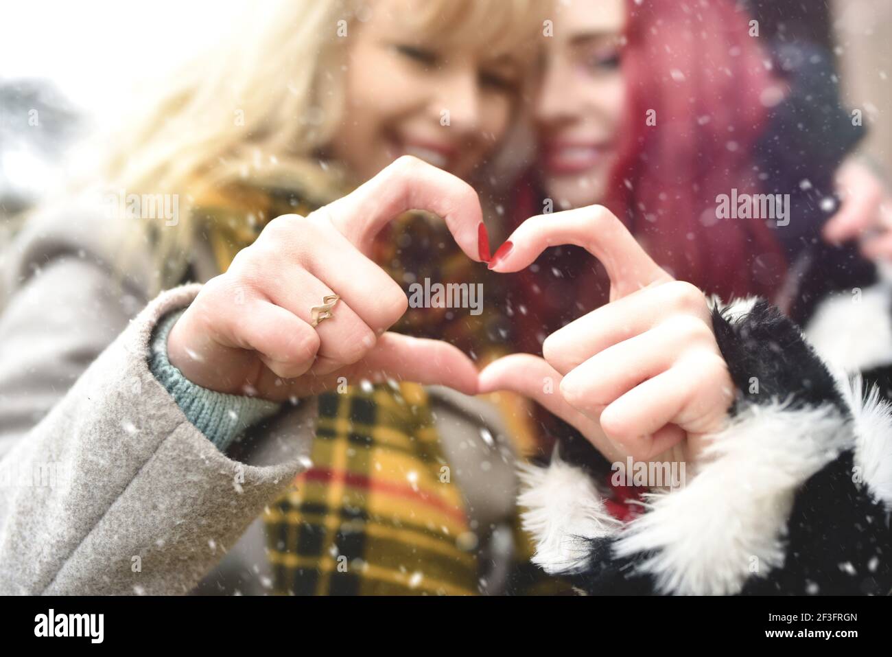 Pareja lesbiana haciendo el corazón con las manos, relación abierta en el amor. Concepto de amor. Concepto de amistad. Efecto nevado Foto de stock