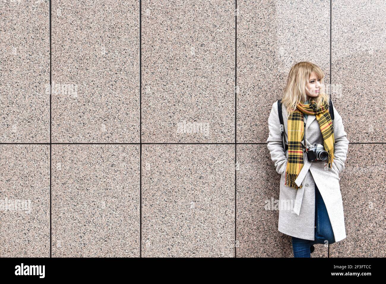 una mujer rubia con una cámara retro se pone de pie contra la pared y mira lejos. espacio libre. espacio de copia Foto de stock