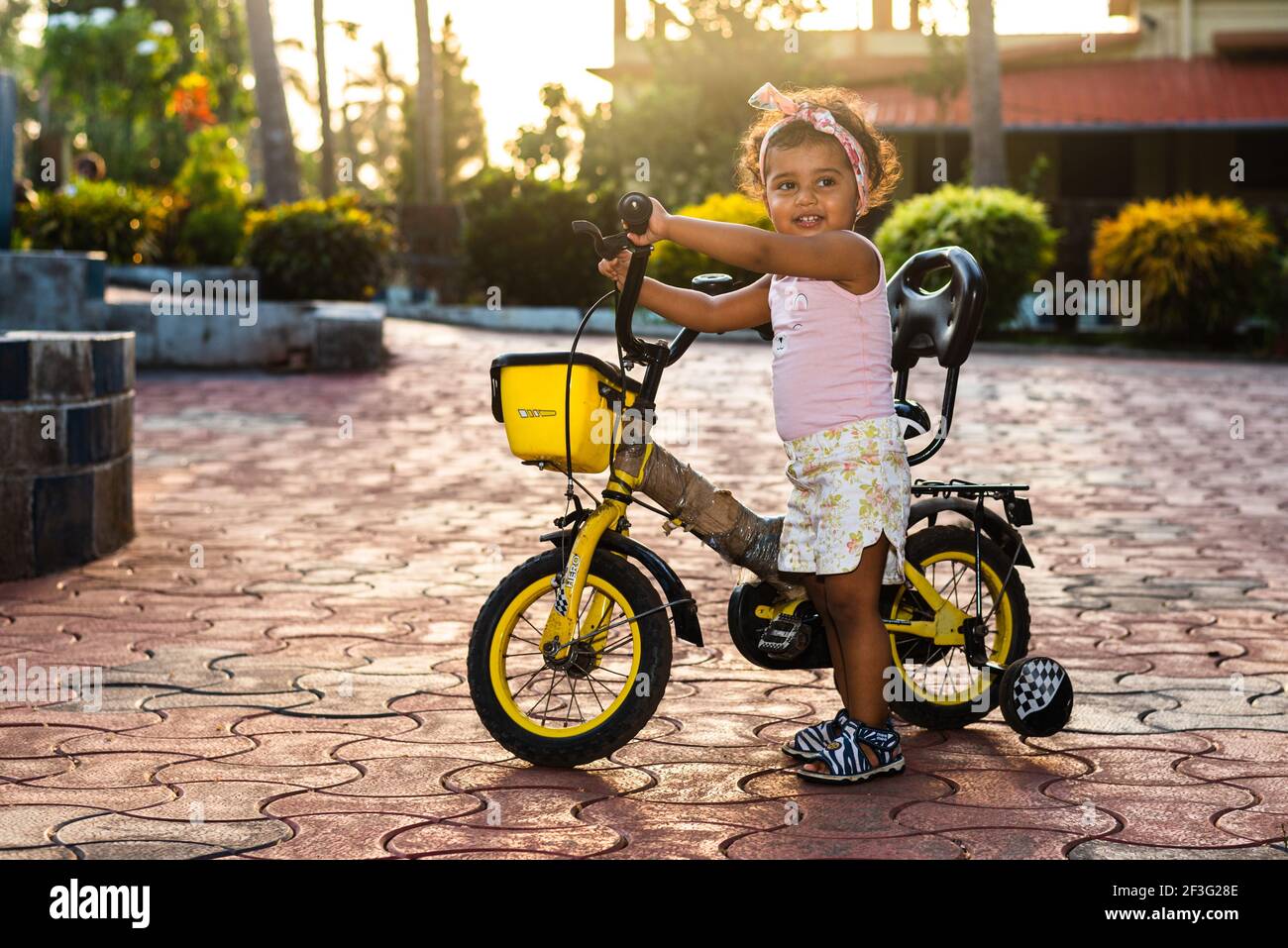 GOA, INDIA - 12 de mayo de 2020: Juguetón Pretty India niña niño/niño/niño  pequeño usando una banda de pelo, jugando con un bicicleta/triciclo. Niño  dando alegría expre Fotografía de stock - Alamy