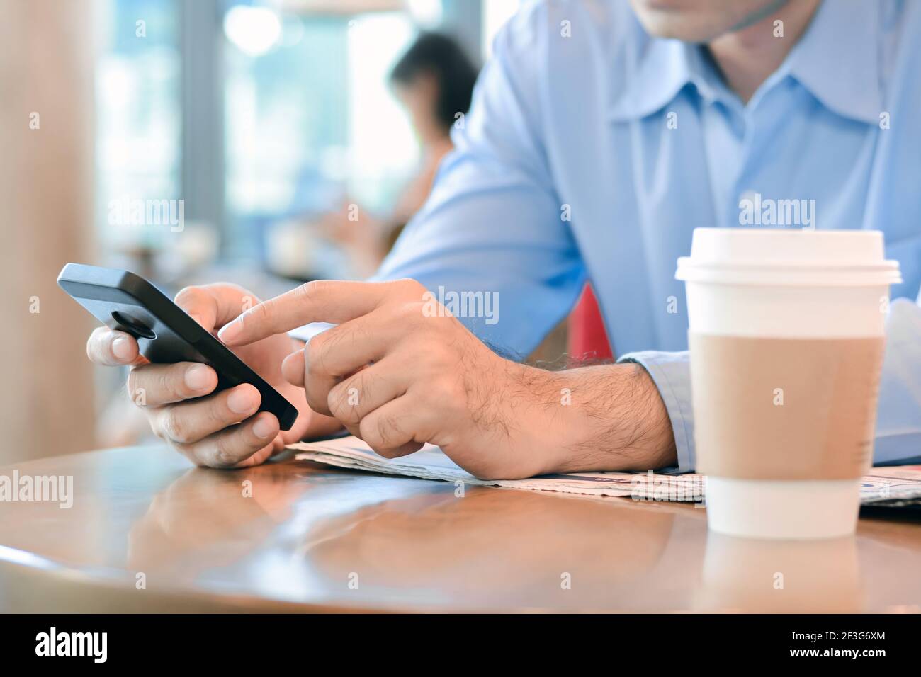 Un hombre que utiliza un teléfono inteligente con una taza de café en el mesa en la cafetería Foto de stock