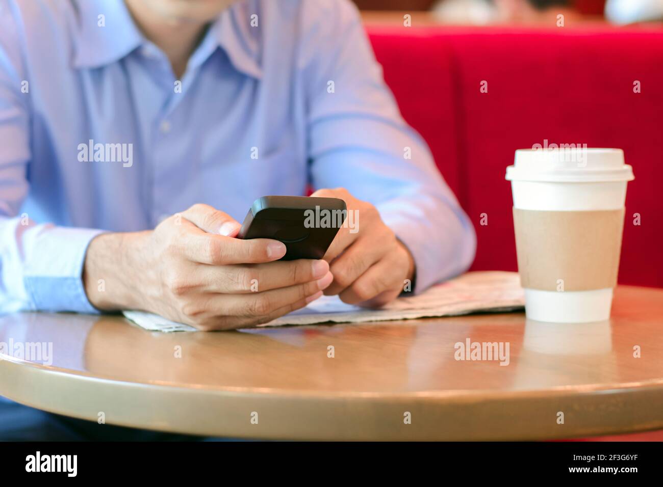 Un hombre que utiliza un teléfono inteligente con una taza de café en el mesa en la cafetería Foto de stock