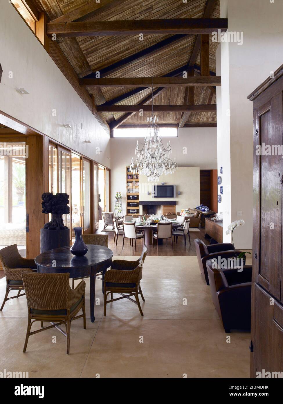 Área de estar de planta abierta con techo con vigas, mesas, sillas y araña de cristal en casa residencial, Brasil. Foto de stock