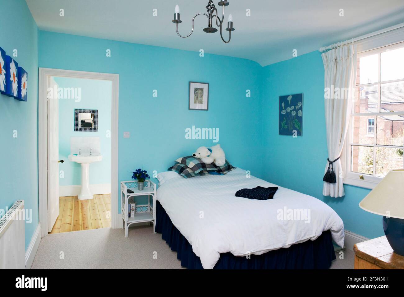 Un moderno dormitorio con paredes azules brillantes, cama, cortinas blancas y baño en-suite Foto de stock