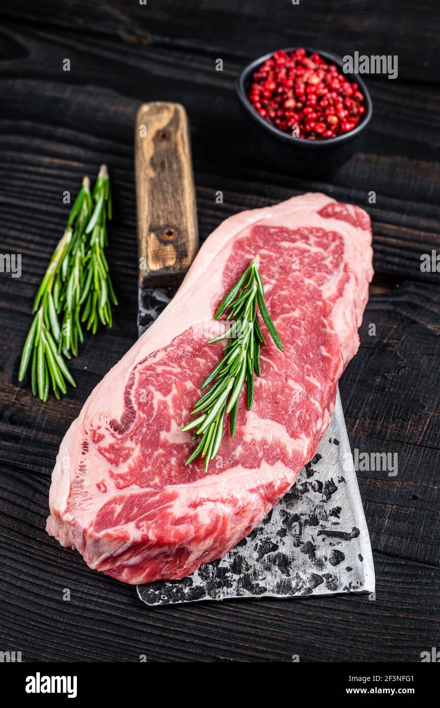 Filete de carne fresca de vaca de la tira de Nueva york en un deshesador de carne de carnicero. Fondo de madera negra. Vista superior Foto de stock