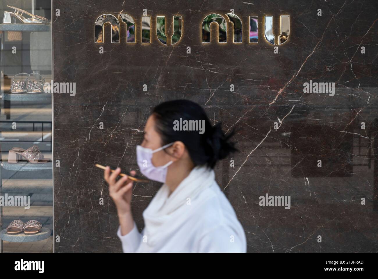 Hong Kong, China. 12th de marzo de 2021. Una mujer que lleva una máscara  mientras usa un smartphone pasa por delante de la tienda italiana de ropa  para mujer de alta moda