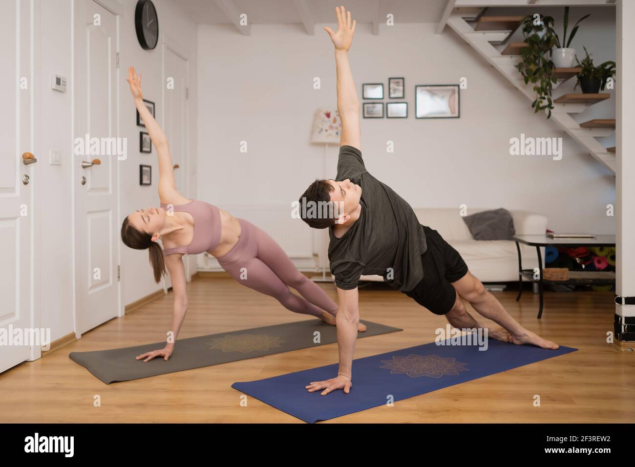 Pareja joven practicando yoga juntos en casa en un interior moderno. Afición, unión, estilo de vida saludable Foto de stock