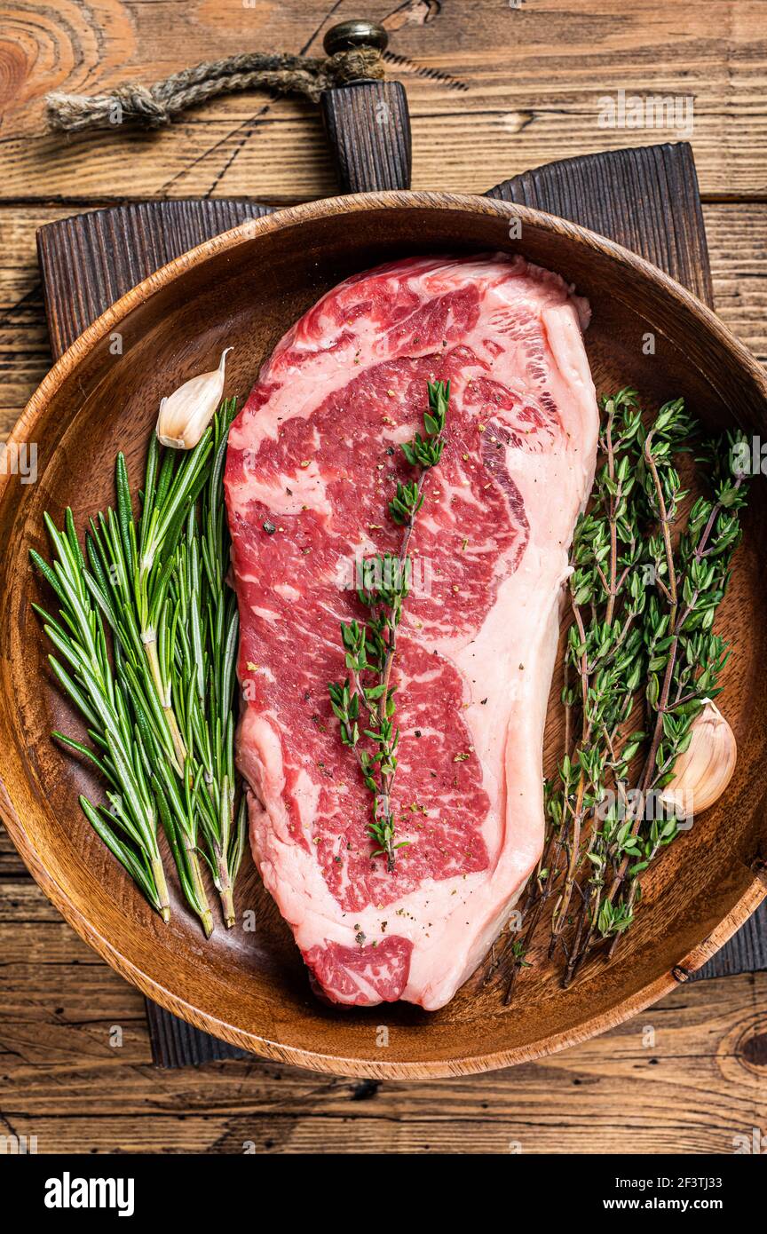 Nueva york tira carne de ternera filete o striploin fresco en un plato de madera con hierbas. Fondo de madera. Vista superior Foto de stock