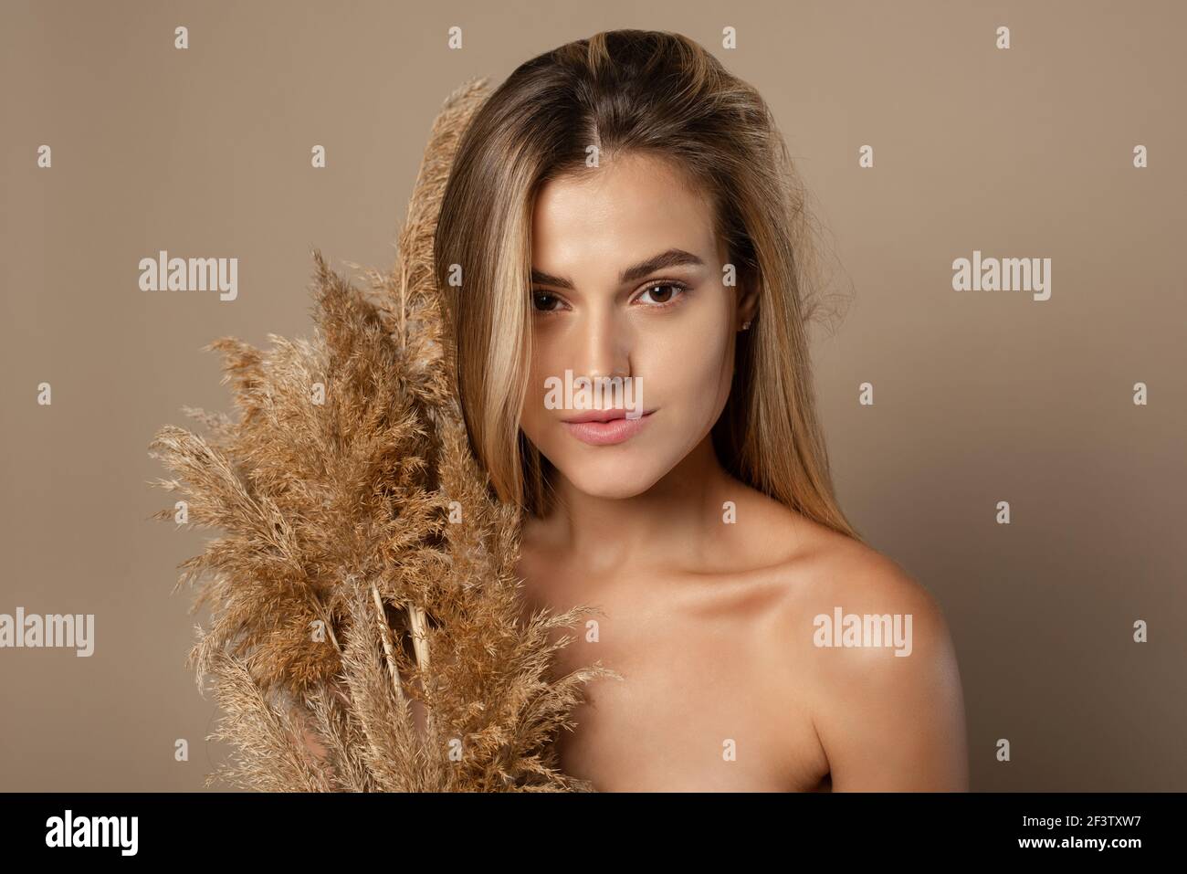 Encantadora joven modelo femenino con pelo suelto sostiene hierba de pampas secas en sus manos. El concepto de cosméticos naturales a partir de granos de trigo. Cuidado de la piel. Foto de stock