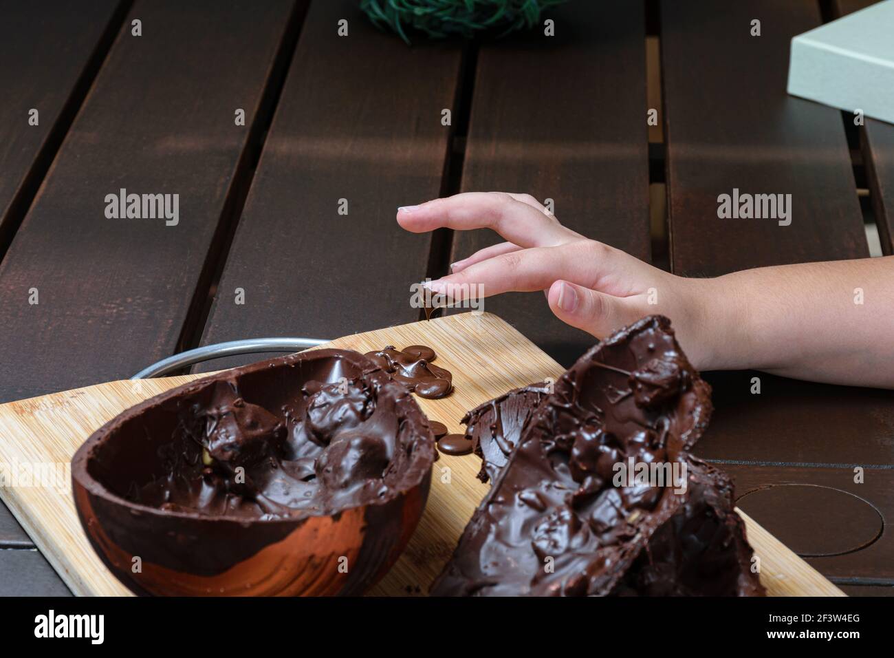 Niño derretir su dedo con chocolate derretido. En primer plano, chocolate negro huevo de Pascua con almendras crujientes. Foto de stock