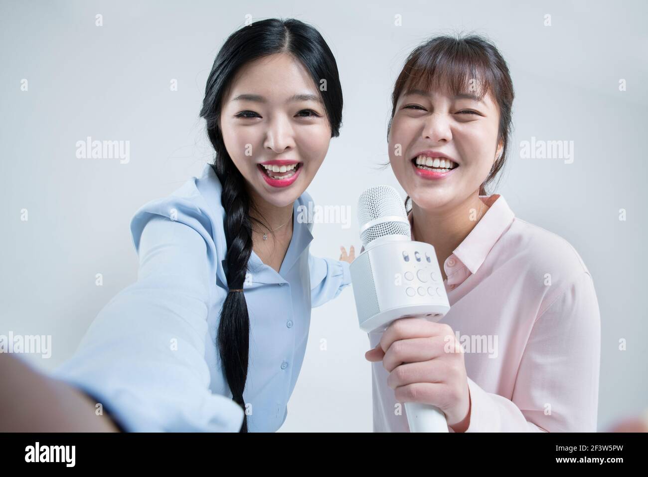Dos mujeres asiáticas, hermanas cantando con micrófono inalámbrico y  aplicación móvil de karaoke en el teléfono Fotografía de stock - Alamy