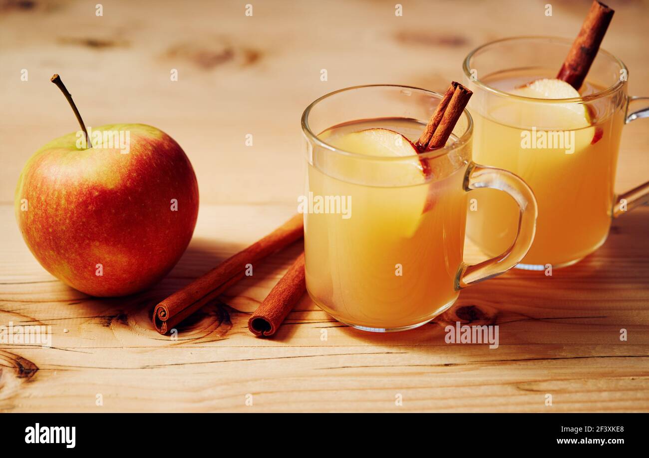 Sidra de manzana casera en una taza de vidrio con canela y.. una rebanada de manzana sobre una mesa de madera Foto de stock