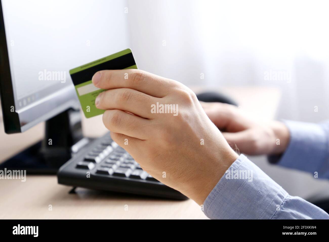 Hombre que sostiene tipos de tarjeta bancaria de crédito en el teclado del PC. Concepto de compra y pago en línea, transacción financiera Foto de stock