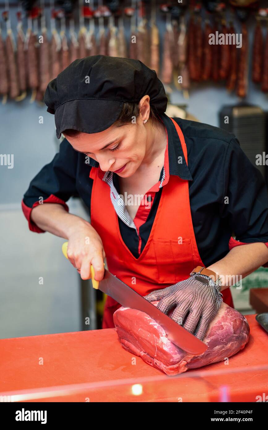 Carnicero hembra cortando carne fresca en un carnicero con guante metálico de seguridad. Mujer carne fresca en una carnicería con guante metálico de malla de seguridad Fotografía de stock -