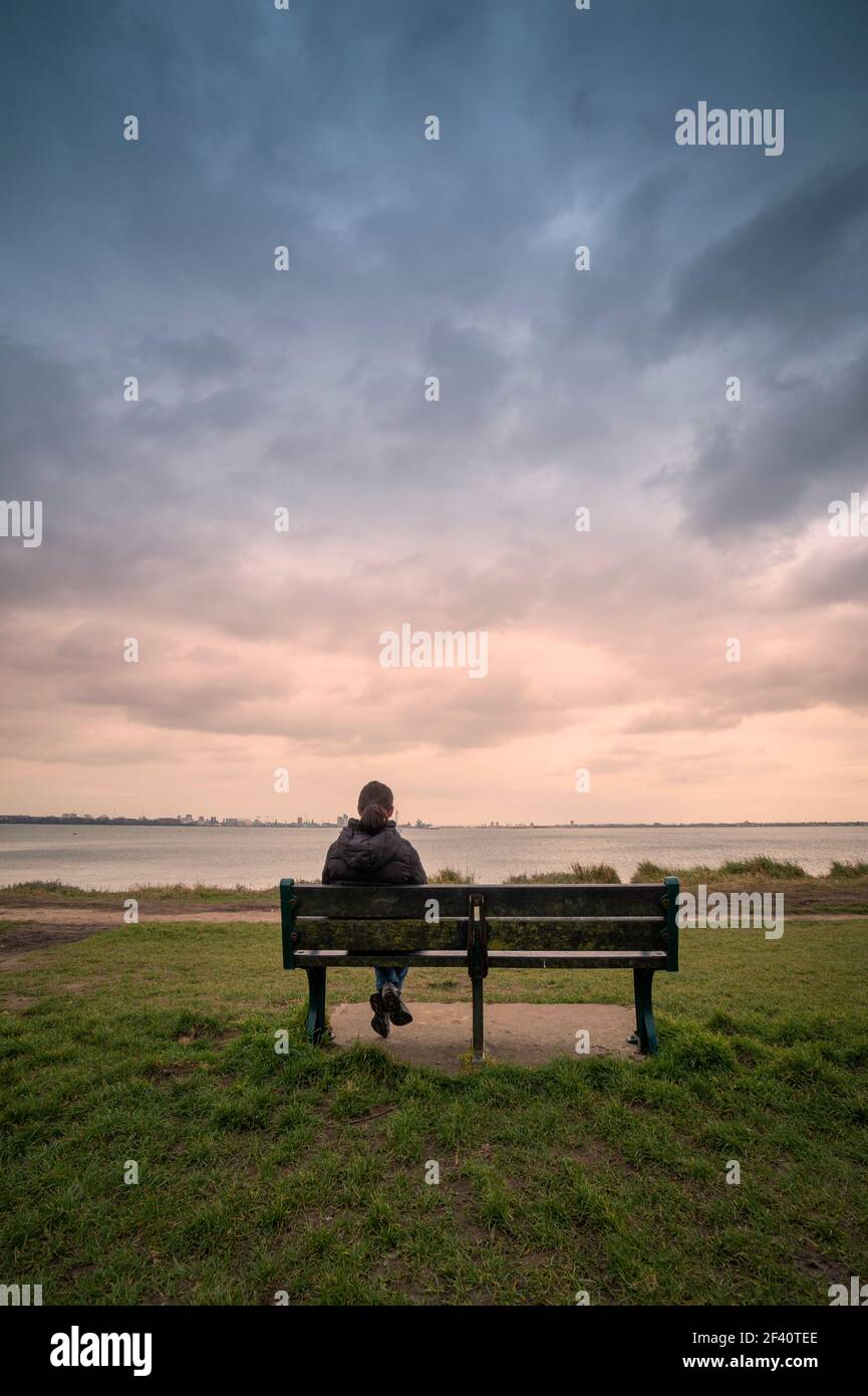 Vista posterior de una mujer sentada en un banco, mirando al mar, cielo estrellado. Foto de stock