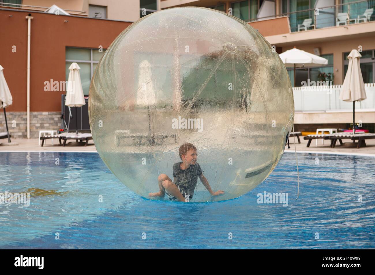 Los niños se divierten dentro de un gran globo de plástico en el agua de la  piscina en el resort de verano. Pequeño niño dentro de la bola transparente  inflable grande runnin