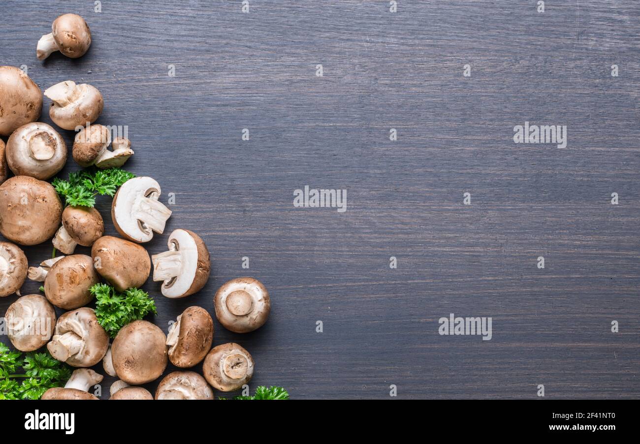 Champiñones comestibles de color marrón o champiñones cremini sobre mesa negra con hierbas. Vista superior. Foto de stock