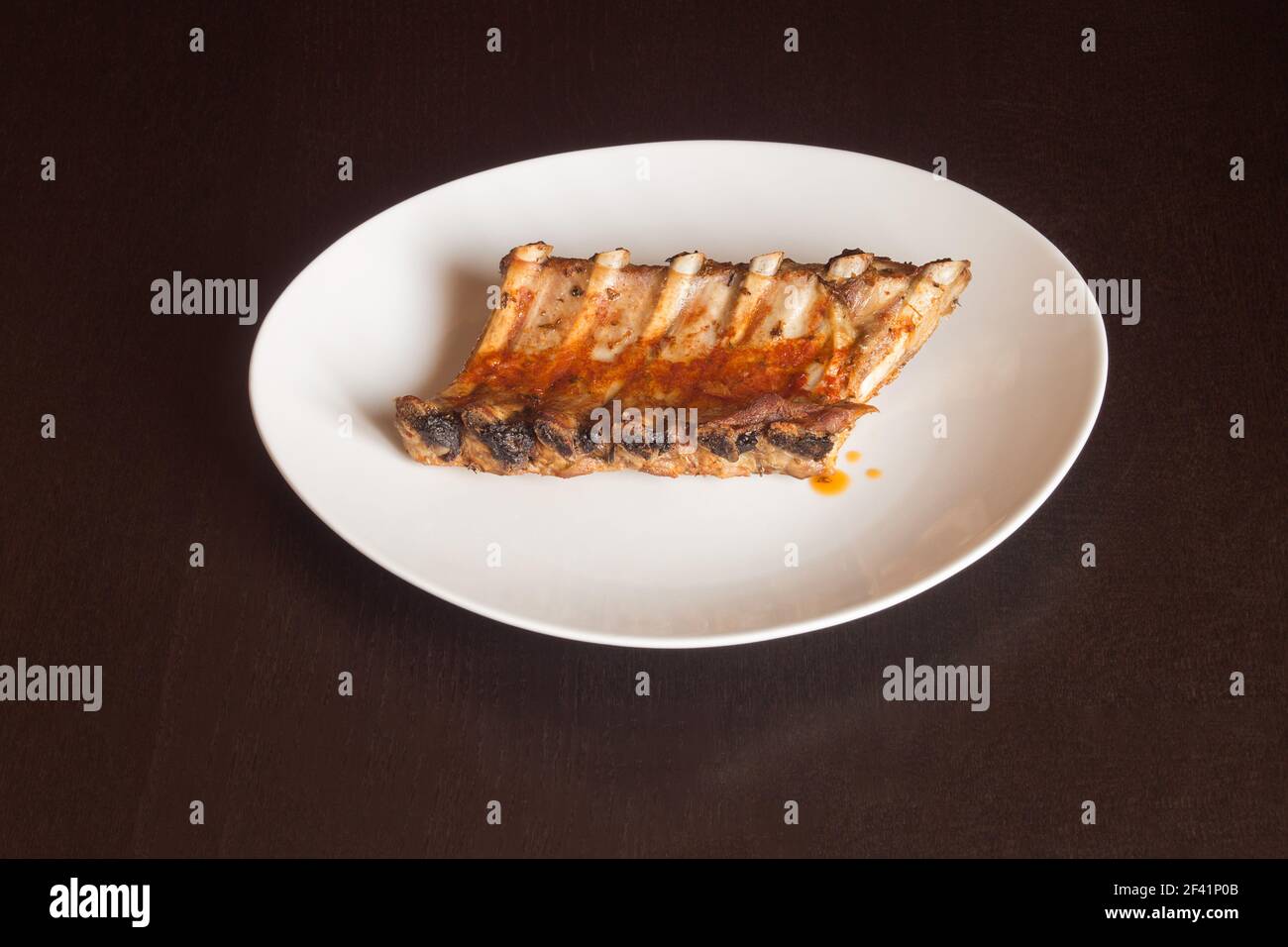 Plato blanco aislado con algunas costillas de cerdo jugosas cocinadas en una salsa picante de verduras sobre una mesa de madera oscura. Comida casera con sabrosa carne. Foto de stock