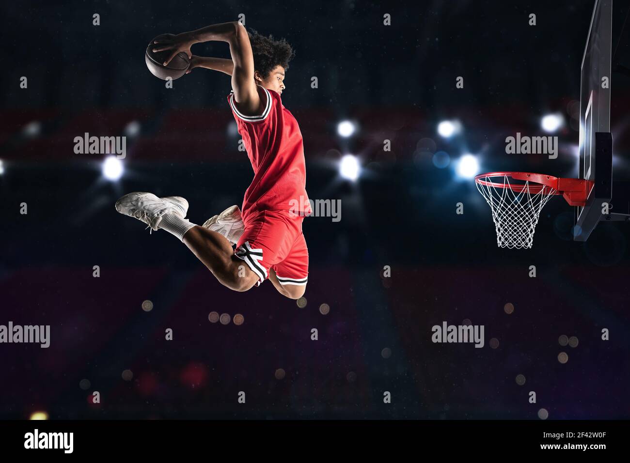 Jugador de baloncesto en rojo uniforme saltando alto para hacer un slam en la cesta Foto de stock
