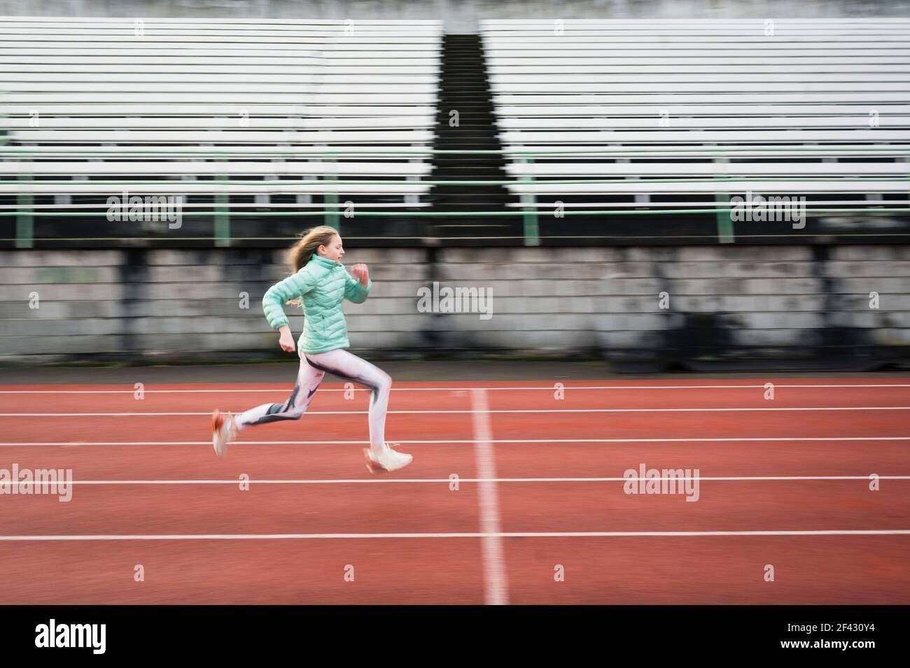 Vista lateral de determinada joven Atlética chica corriendo en rojo Pista Foto de stock