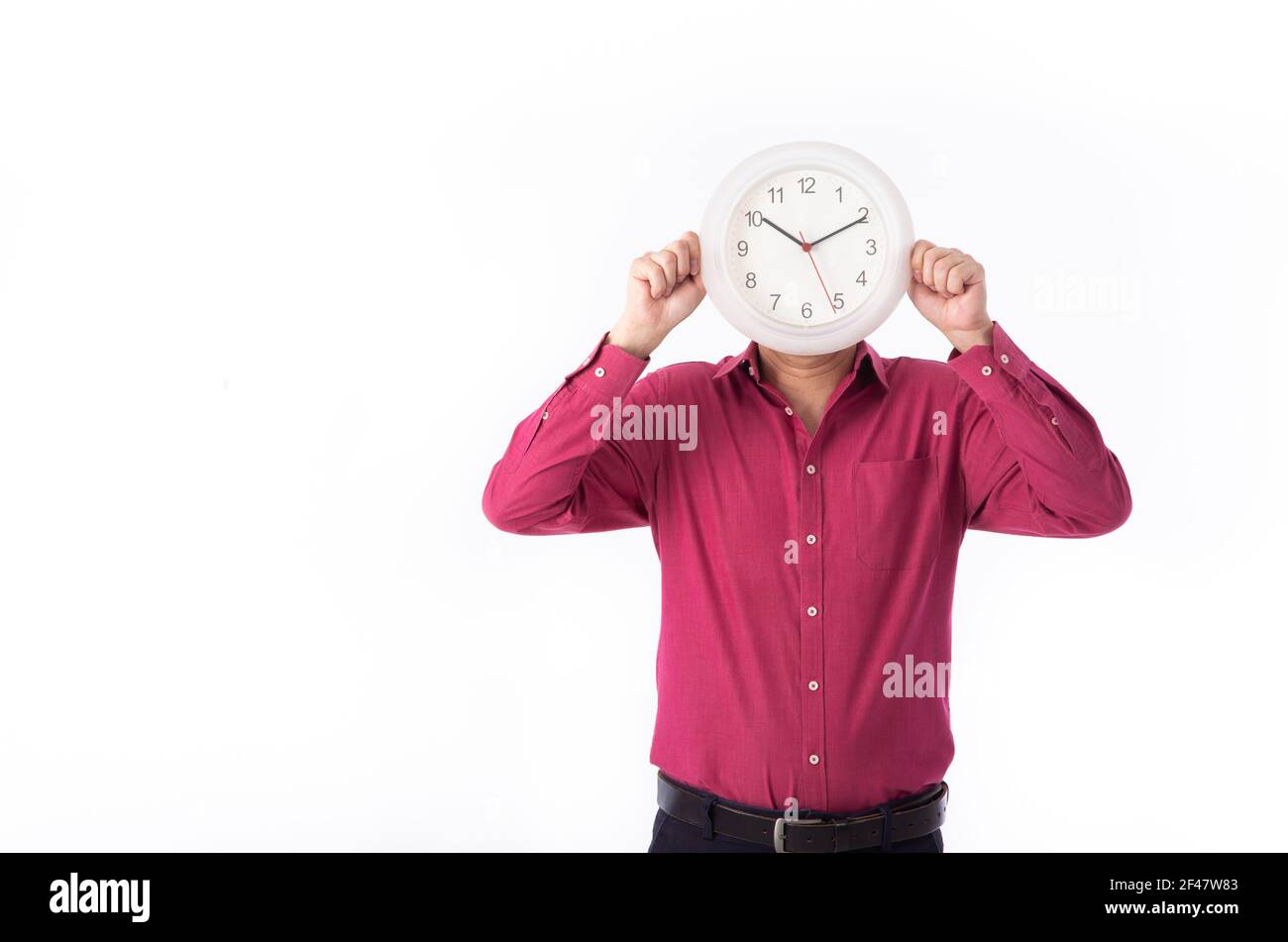 Un hombre de negocios que sostiene un reloj frente a su cara, aislado sobre fondo blanco. Foto de stock