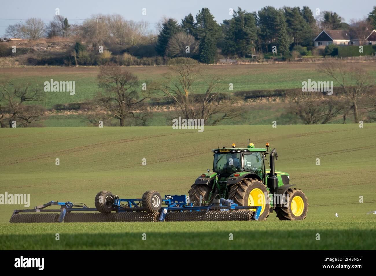 Un tractor John Deere tira de una máquina de preparación de cultivos a través de un campo cultivado, West Lothian, Escocia. Foto de stock