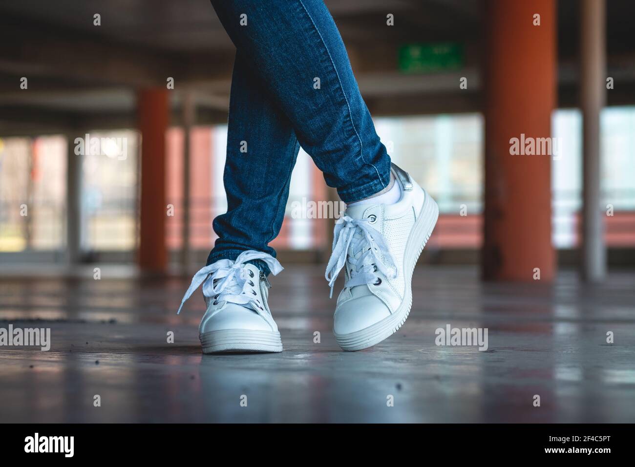 Dinkarville Virus Cabecear Mujer con zapatillas blancas en el garaje público. Concepto de moda.  Piernas delgadas femeninas con jeans y zapatos deportivos en el  aparcamiento Fotografía de stock - Alamy