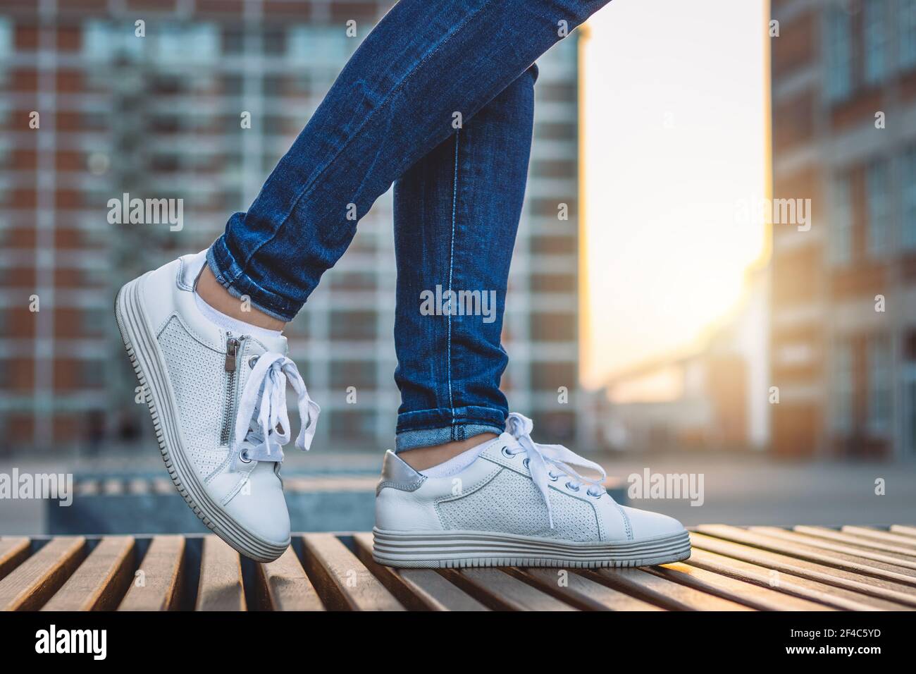 Mujer que lleva jeans y zapatillas blancas está de pie en la ciudad después  de la puesta de sol. Moda y concepto elegante. Arquitectura moderna como  fondo Fotografía de stock - Alamy