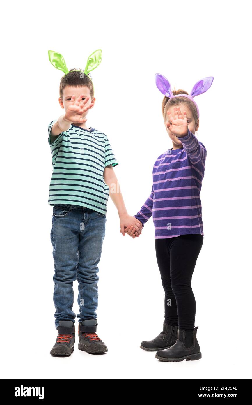 Dos niños niño y niña sosteniendo las manos agitando con la cámara con orejas de conejito de pascua. Cuerpo entero aislado sobre fondo blanco Foto de stock