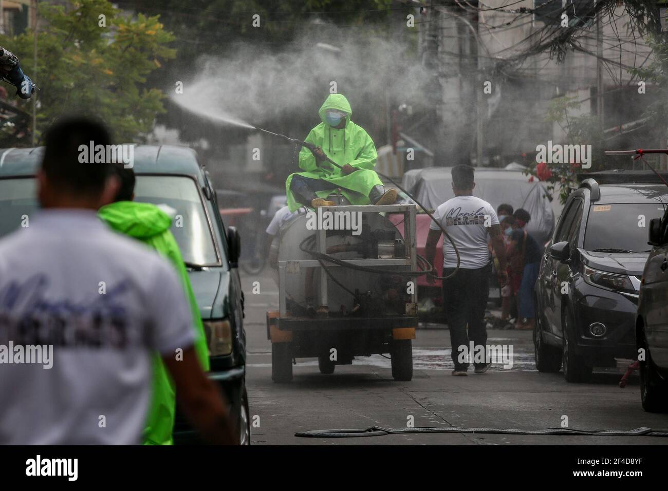 Los trabajadores pulverizan solución desinfectante a lo largo de una calle dentro de una zona residencial, ya que la capital filipina Marca un año bajo una cuarentena comunitaria para ayudar a combatir la propagación del coronavirus. Filipinas. Foto de stock
