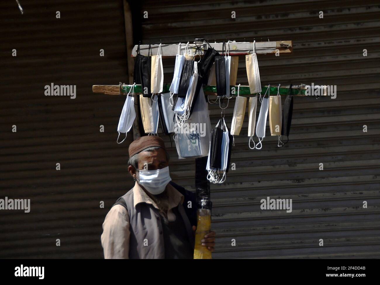 Peshawar. 20th de marzo de 2021. Un vendedor vende máscaras frente a una tienda cerrada en Peshawar, en el noroeste de Pakistán, el 20 de marzo de 2021. Pakistán se enfrenta a una grave tercera ola de virus y el gobierno está tomando medidas para garantizar los procedimientos operativos estándar para controlar la propagación del virus. Crédito: Saeed Ahmad/Xinhua/Alamy Live News Foto de stock