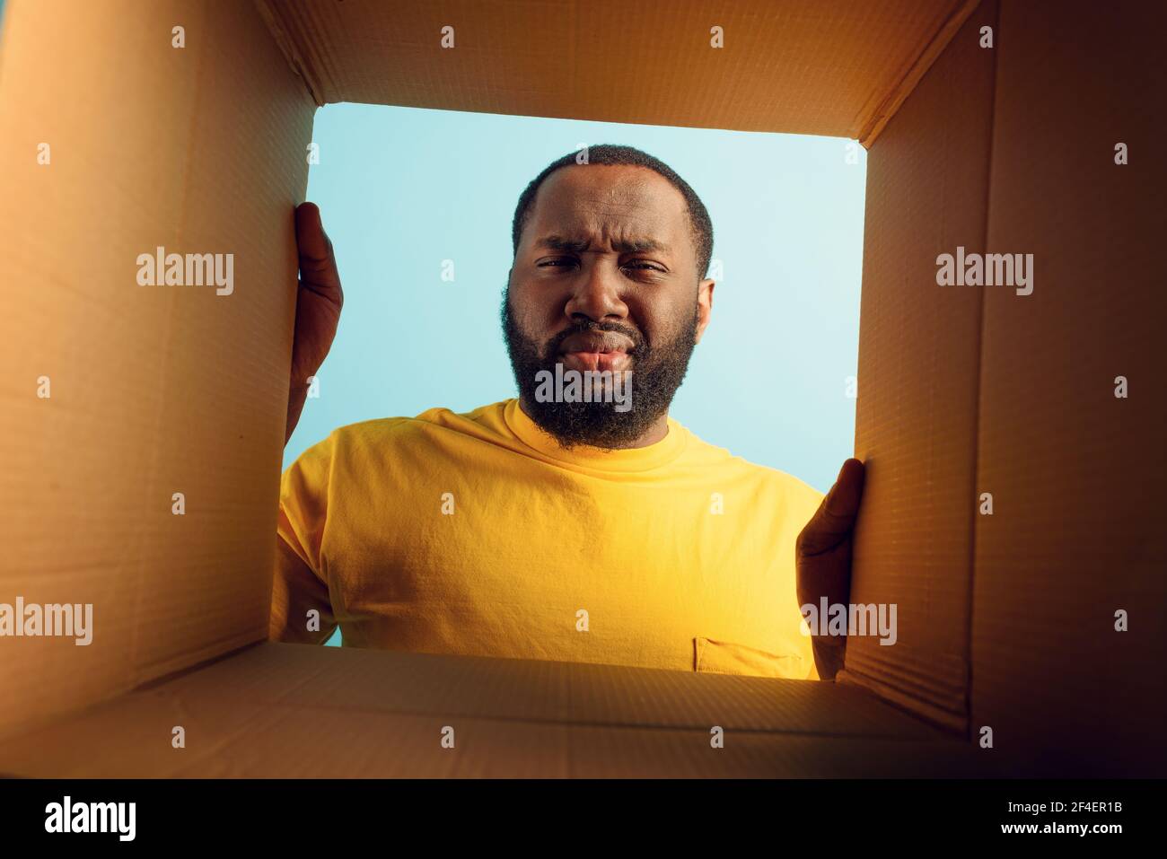 El hombre tiene dudas y está disgustado por lo que hay dentro de un paquete. Concepto de fraude en la tienda en línea Foto de stock