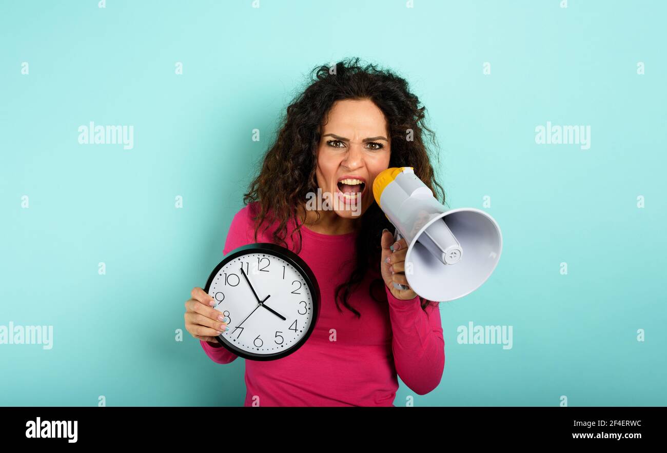 Mujer grita con altavoz porque es demasiado tarde. Expresión enojada. Fondo cian Foto de stock