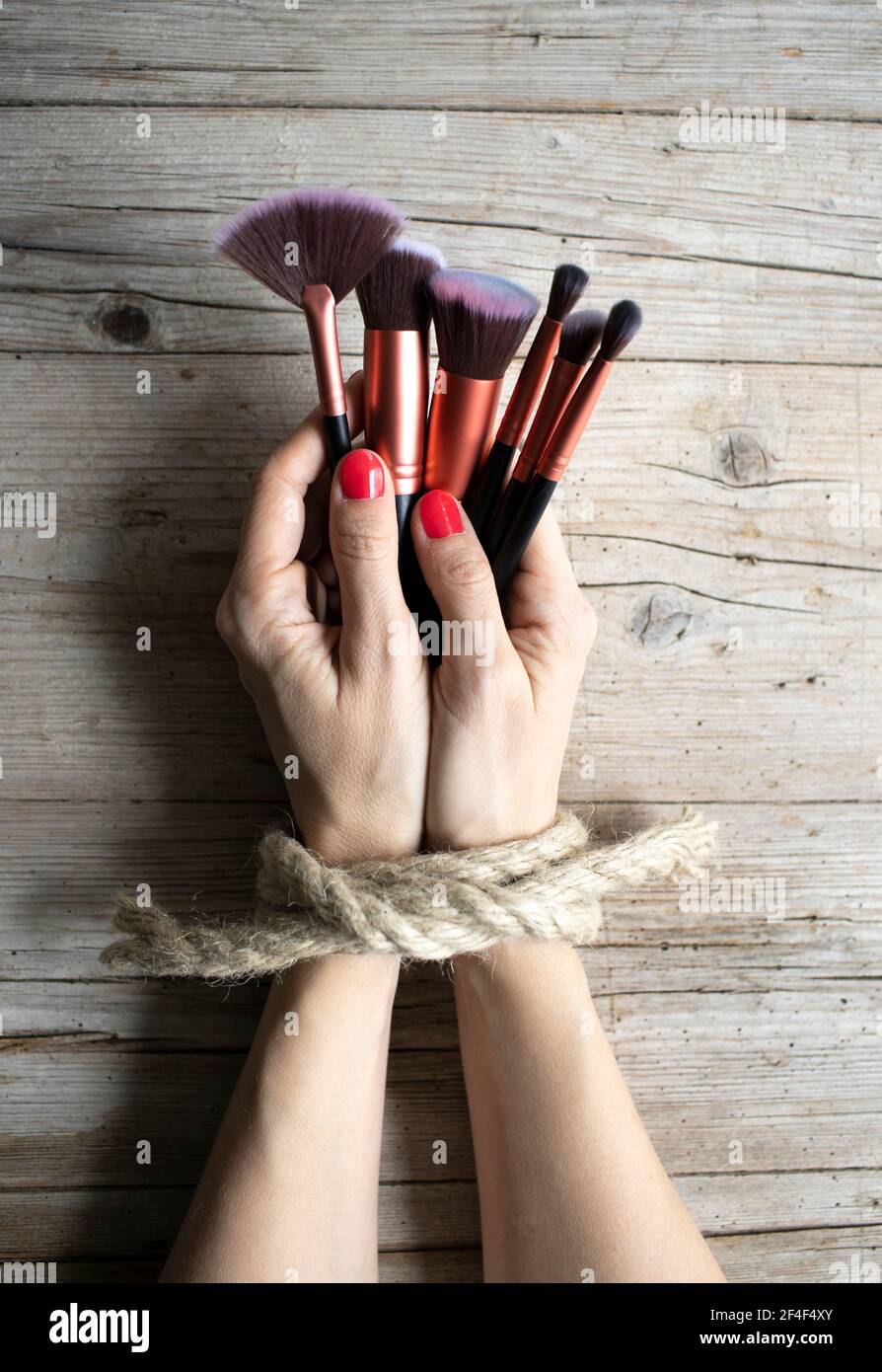 Las manos de la mujer joven con uñas rojas están atadas y yacen sobre un fondo de madera clara, ella sostiene cepillos de maquillaje, concepto sobre la adicción, la manía de la belleza Foto de stock