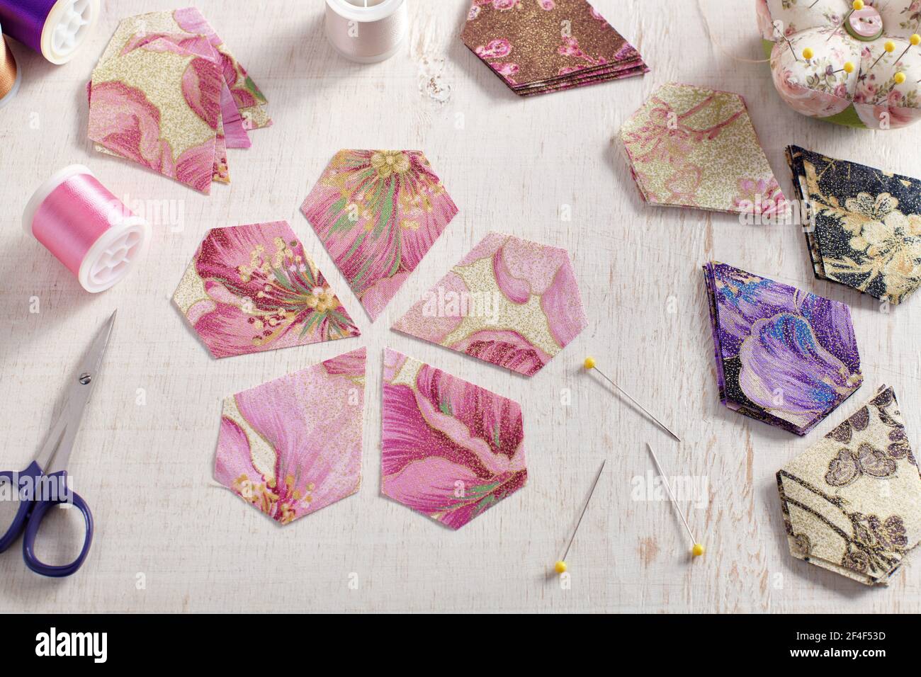 Piezas pentagonal de tela en forma de flor, pilas de piezas de tela multicolor, accesorios de costura sobre una superficie blanca Foto de stock