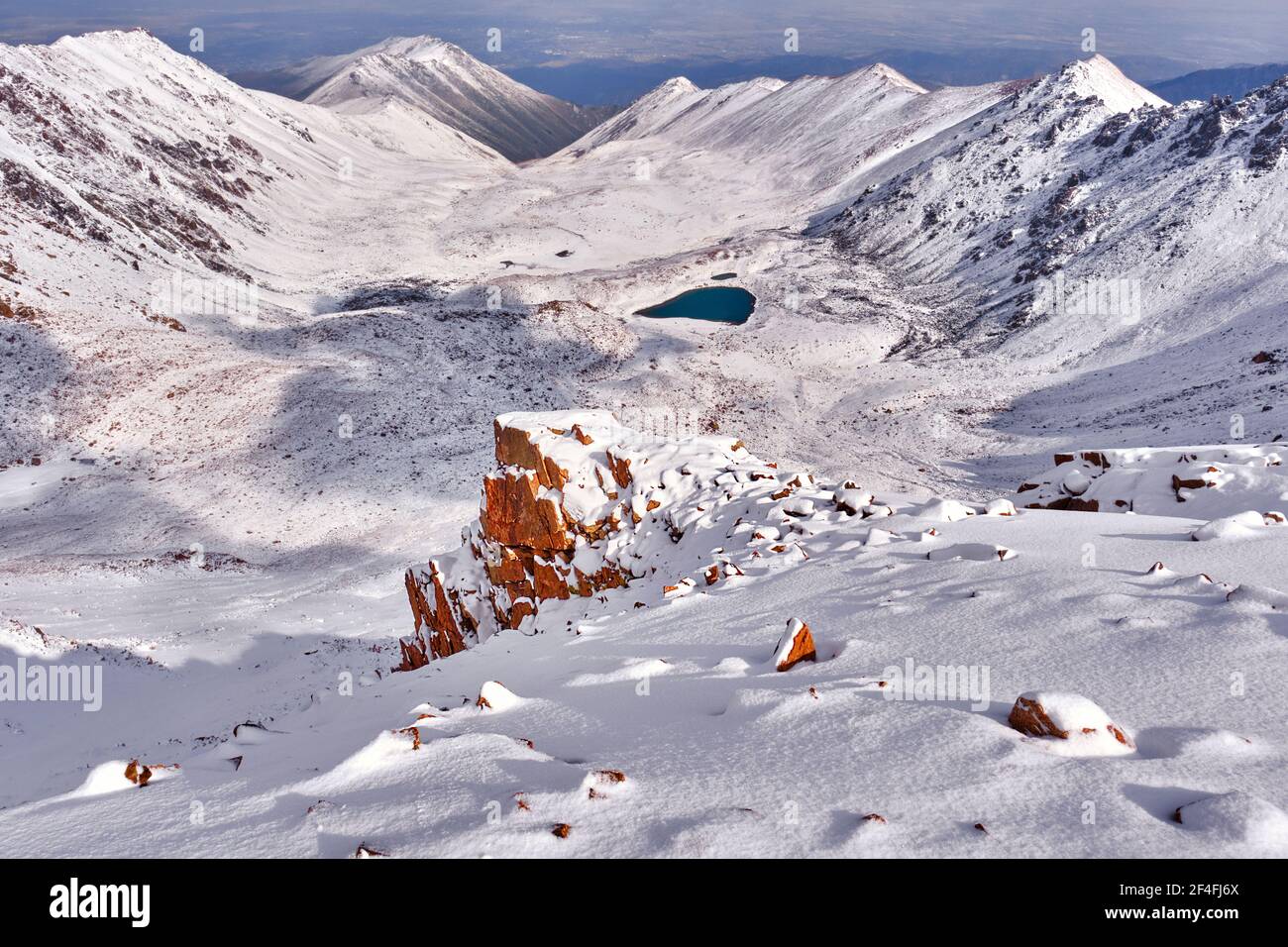 Épica vista por la mañana de un valle de montaña con lagos moraine después de una Nevada nocturna; la primera nieve en las montañas con el cercano mar de invierno Foto de stock