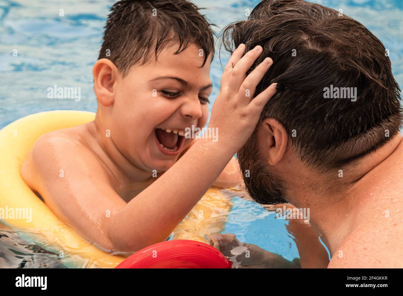 niño discapacitado con un flotador se ríe mientras juega y.. nada en una  piscina con su padre Fotografía de stock - Alamy