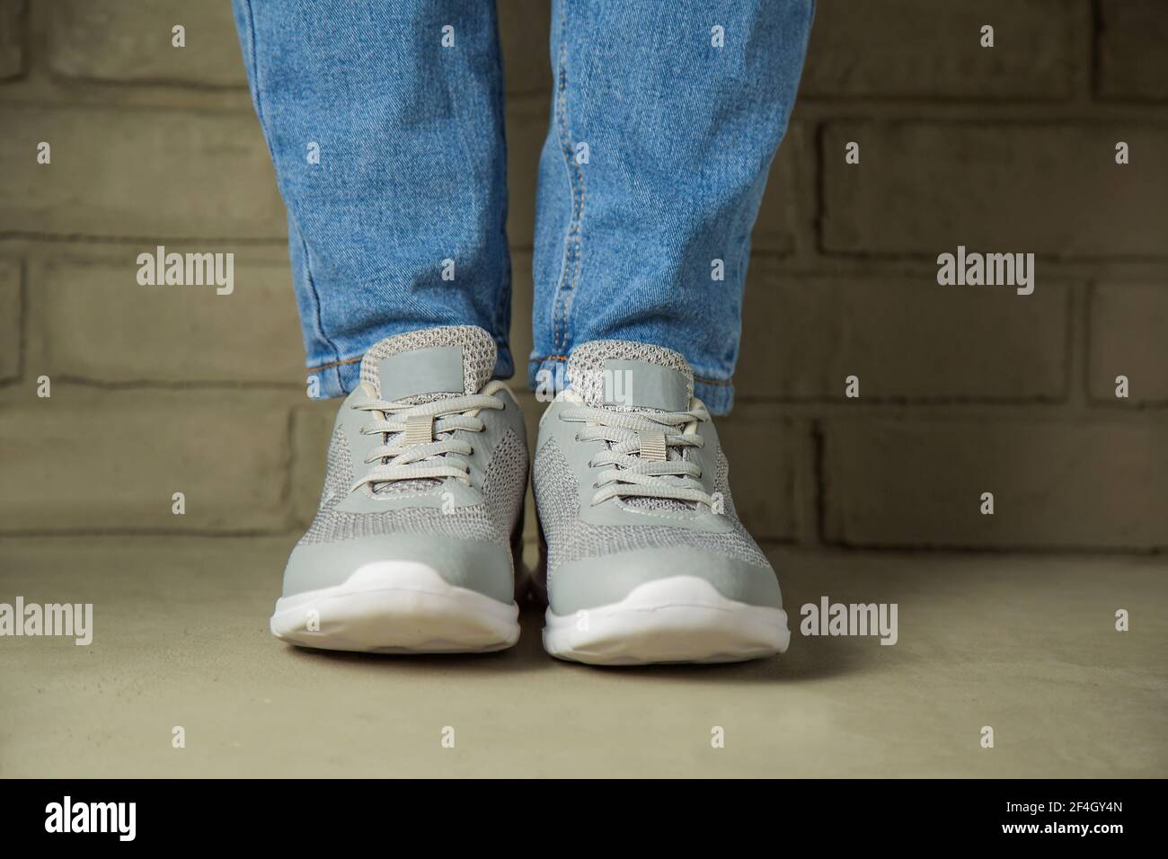Una mujer en sneakers blancas está contra una pared de ladrillo en el  fondo. Pies en zapatos deportivos sin Marca Fotografía de stock - Alamy
