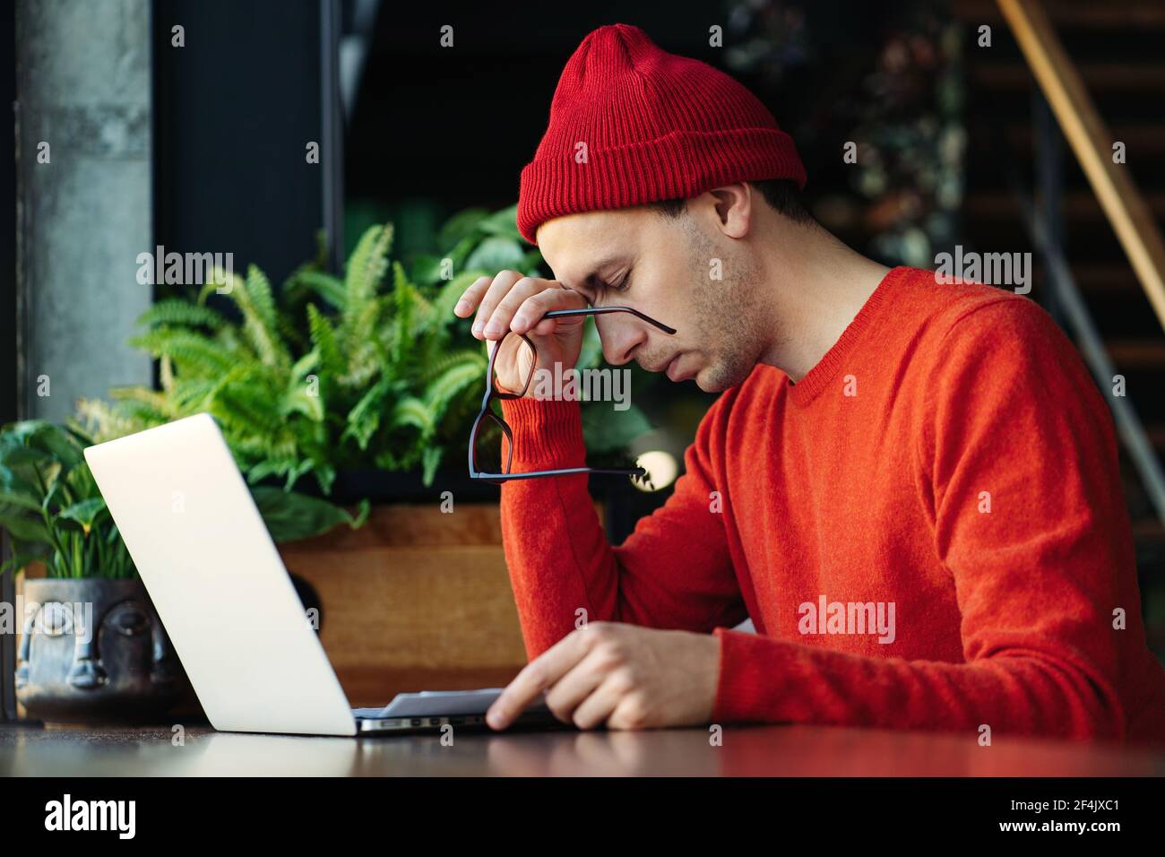 Hombre cansado tomando un descanso durante el trabajo en línea en el portátil, sosteniendo la cabeza en la mano, sintiendo falta de energía. Foto de stock