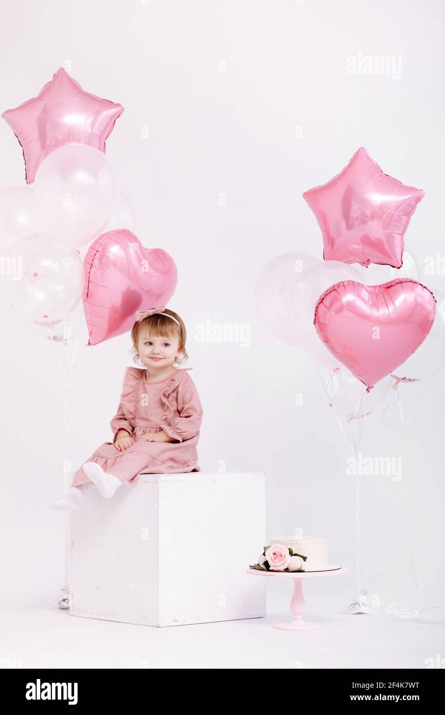 feliz cumpleaños niña de 2 años con vestido rosa. pastel blanco con velas y  rosas. Decoración de cumpleaños con globos de color blanco y rosa y  Fotografía de stock - Alamy