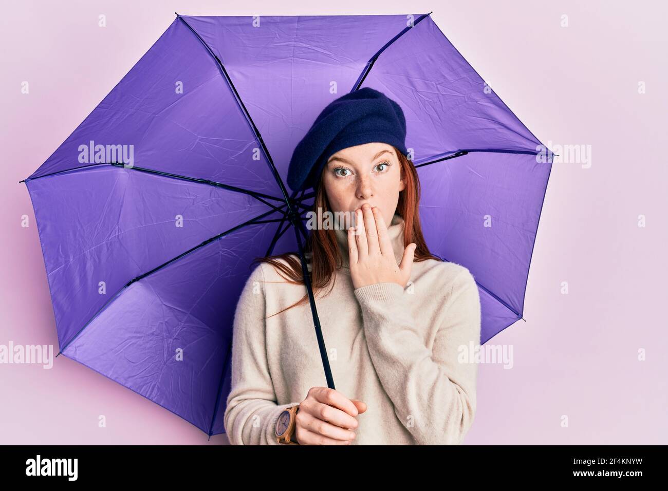 Joven rojo cabeza niña sosteniendo paraguas púrpura con bereta fresca  cubriendo la boca con la mano, conmocionado y asustado por error. Expresión  sorprendida Fotografía de stock - Alamy