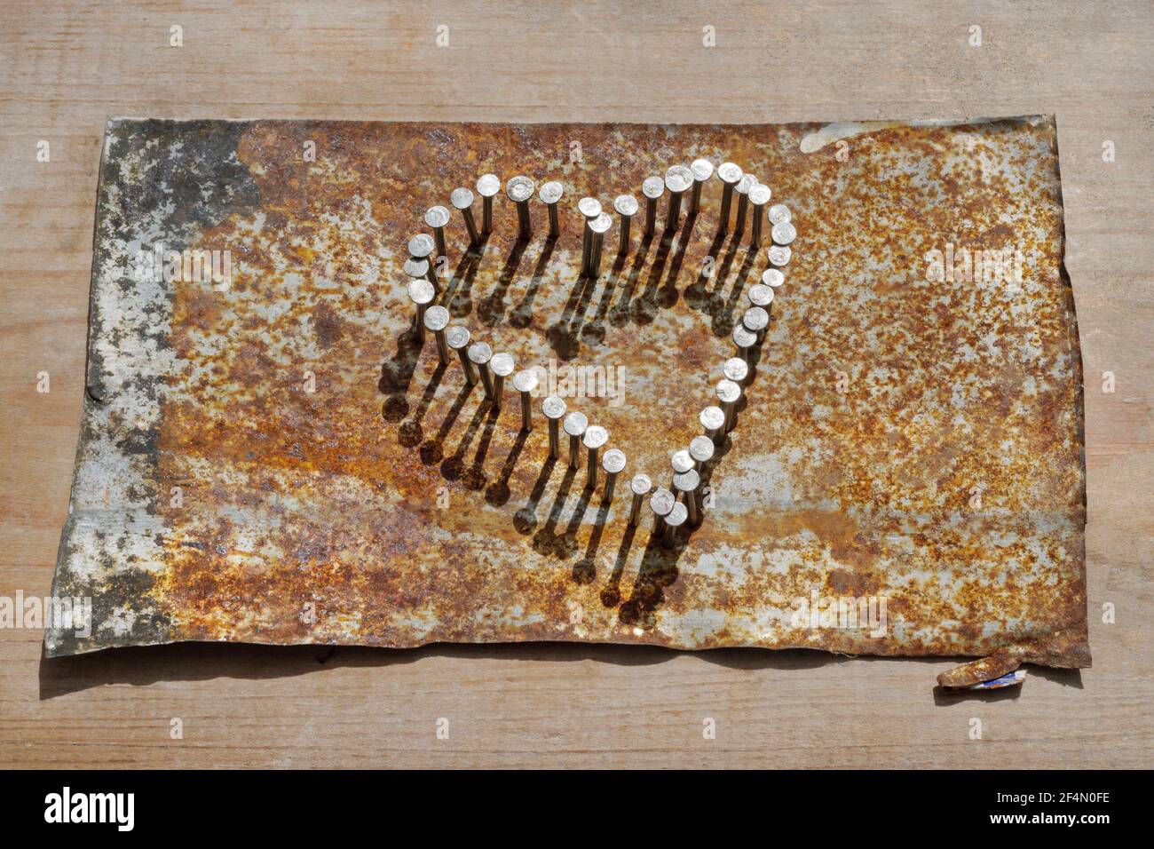 Corazón de uñas martilladas en estaño oxidado aplanado sobre tabla de madera. Foto de stock
