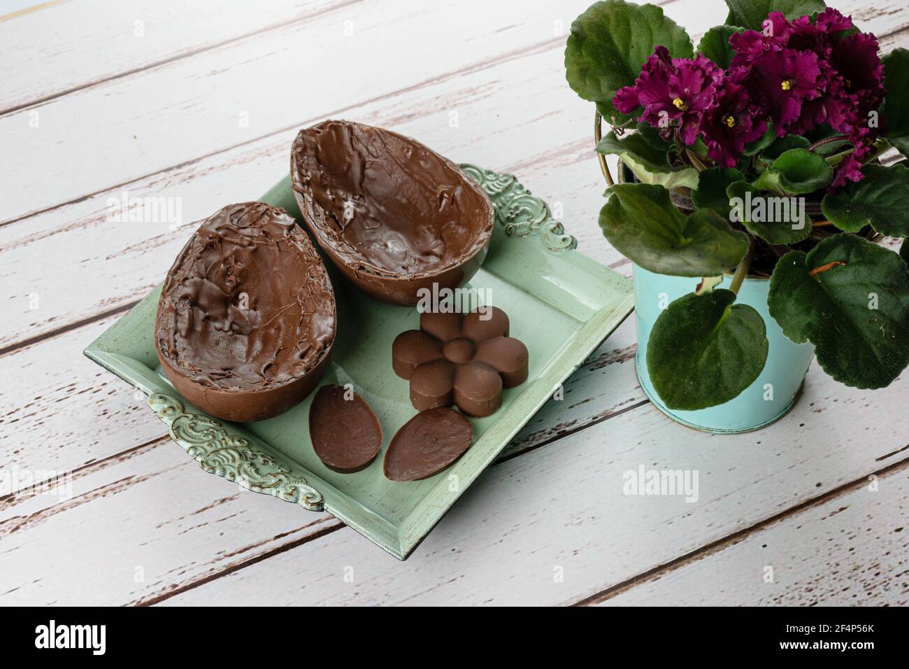 Dos mitades de chocolate huevo de Pascua, en una pequeña bandeja antigua junto a mini chocolates y flores. Foto de stock