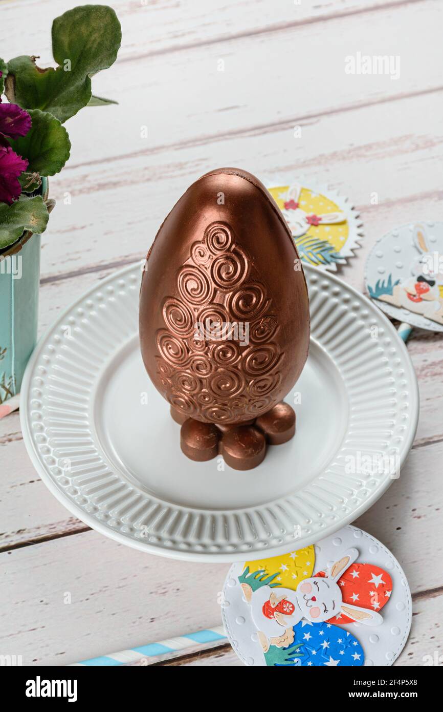 Huevo de Pascua de chocolate decorado con pintura de color cobre comestible. Sobre una mesa de madera blanca. Foto de stock