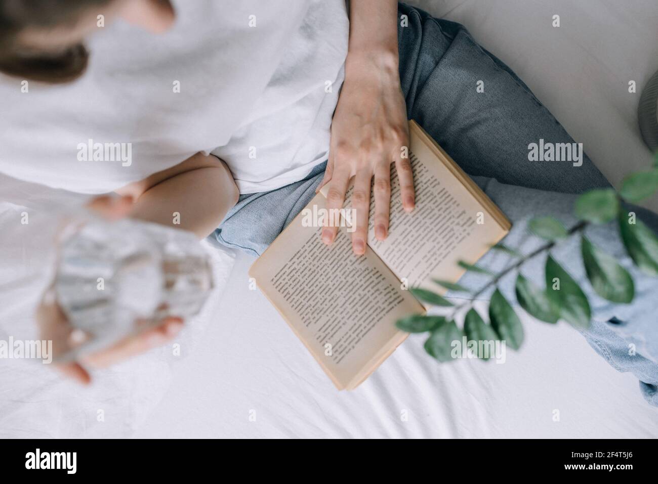 Una mujer joven leyendo un libro en una cama y. con un vaso de vista de la cima del agua Foto de stock