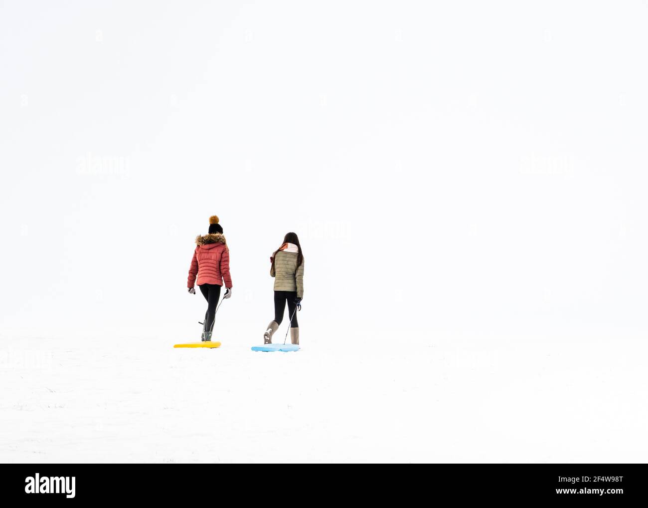 En un invierno whiteout dos niñas / mujeres jóvenes tirar trineos en la nieve Foto de stock