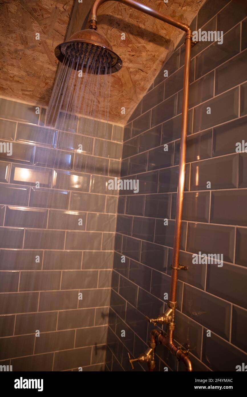 Rociado de agua del cabezal de ducha de cobre en la ducha de azulejos Foto de stock