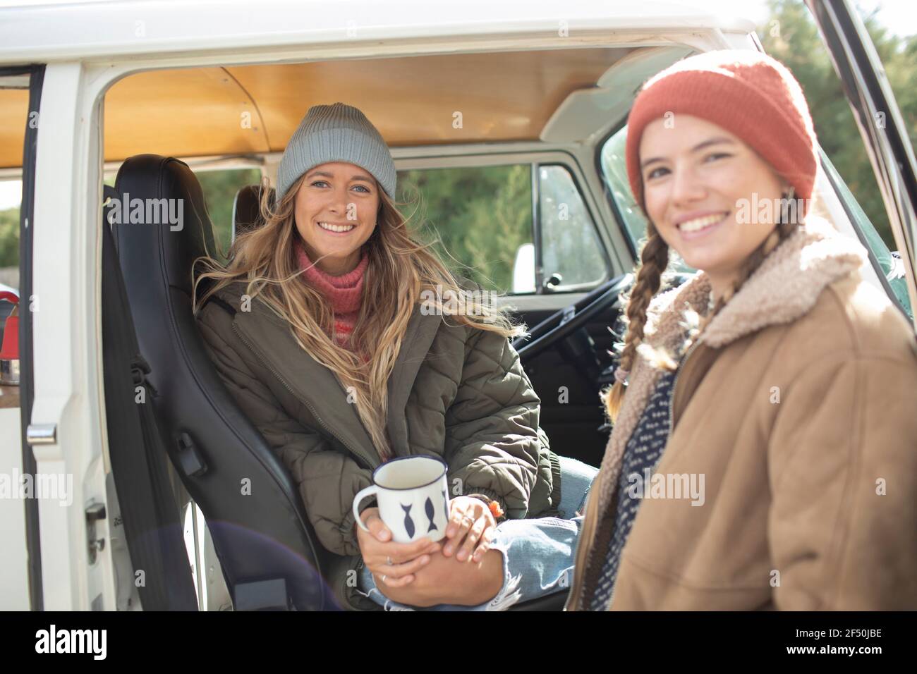 Retrato felices jóvenes amigas tomando café en la puerta de la furgoneta Foto de stock