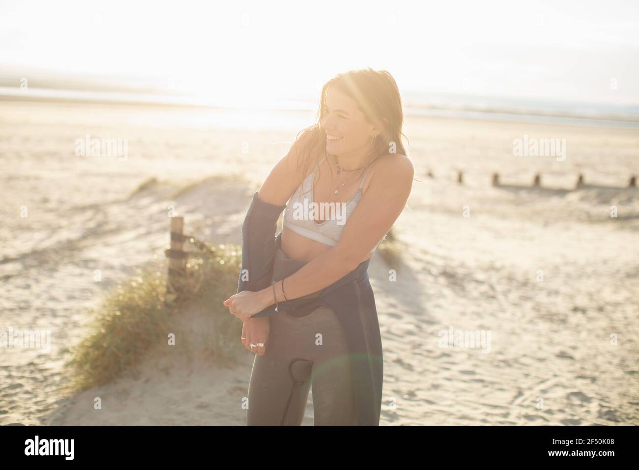 Joven surfista mujer quitando traje húmedo en la playa soleada Foto de stock