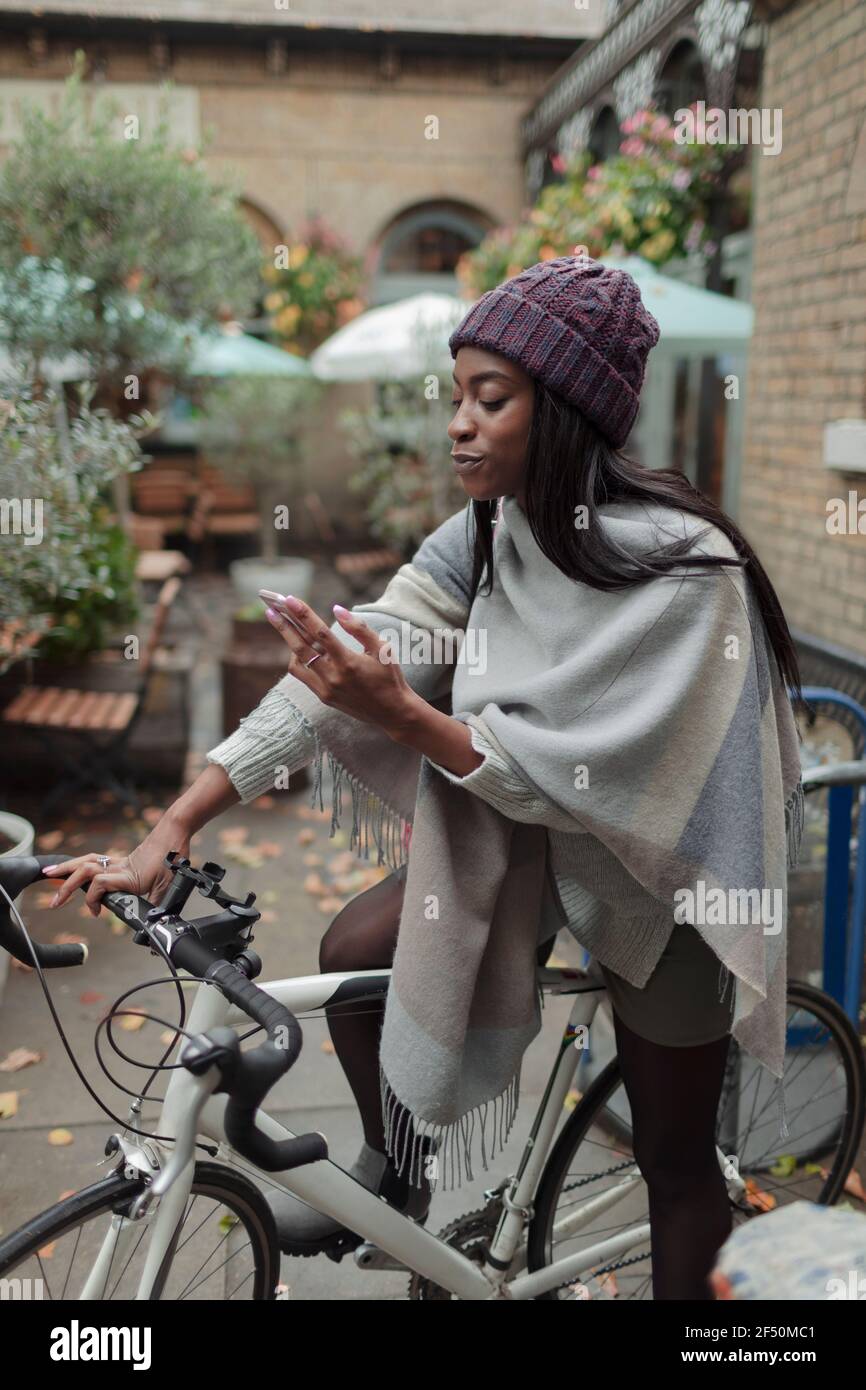 Mujer joven montando una bicicleta eléctrica y utilizando el teléfono móvil